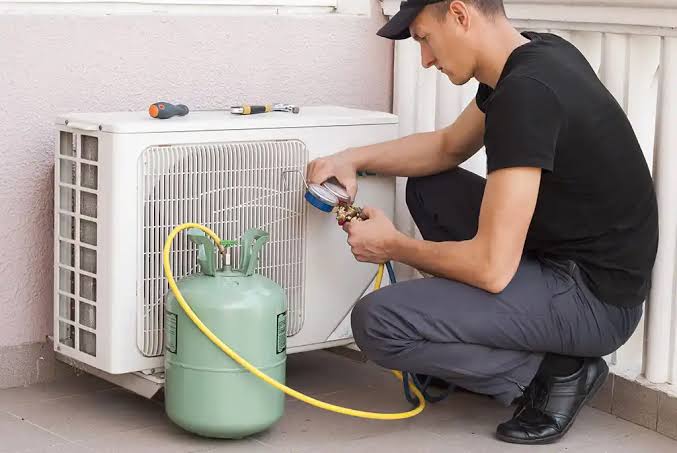 Technician checking service gauges beside a compact outdoor air conditioning unit