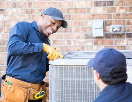 Two technicians examining the top of a residential outdoor HVAC unit
